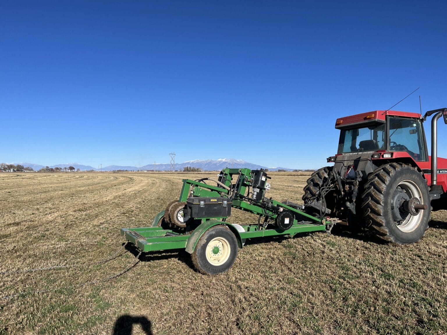 Red tractor with green farm equipment in mountain field