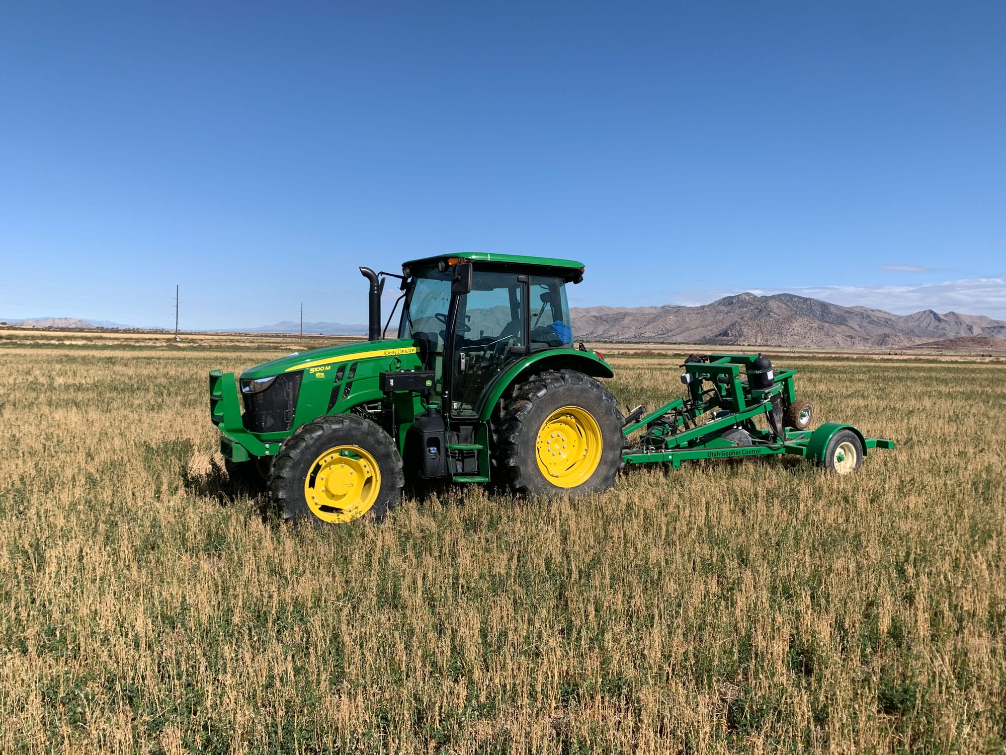 Green John Deere tractor with gopher control equipment in field