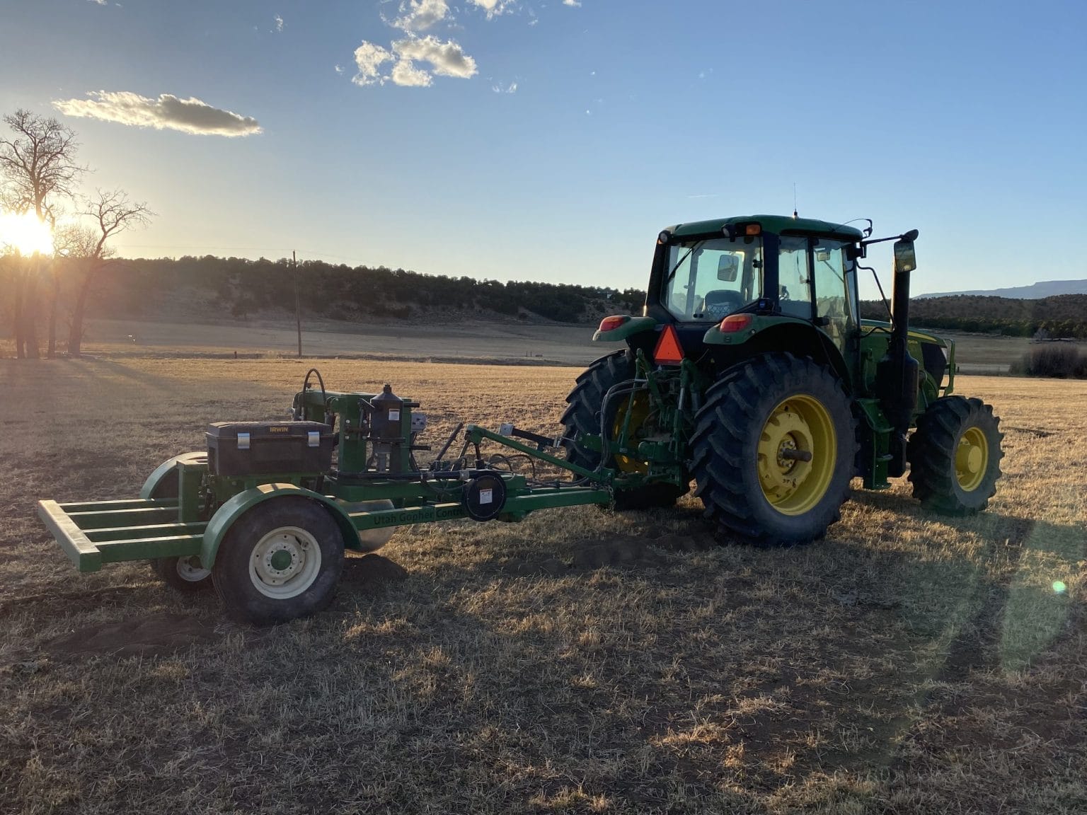 Green tractor with field equipment at sunset