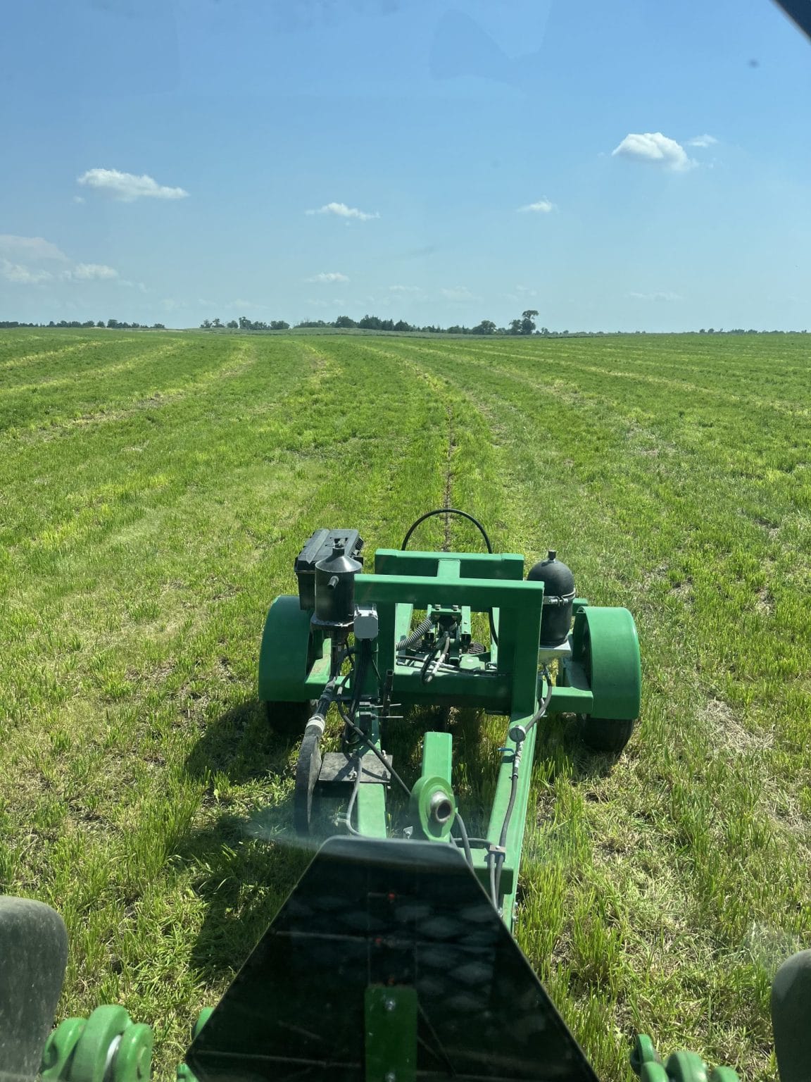 Green farm machinery working in a field under blue sky
