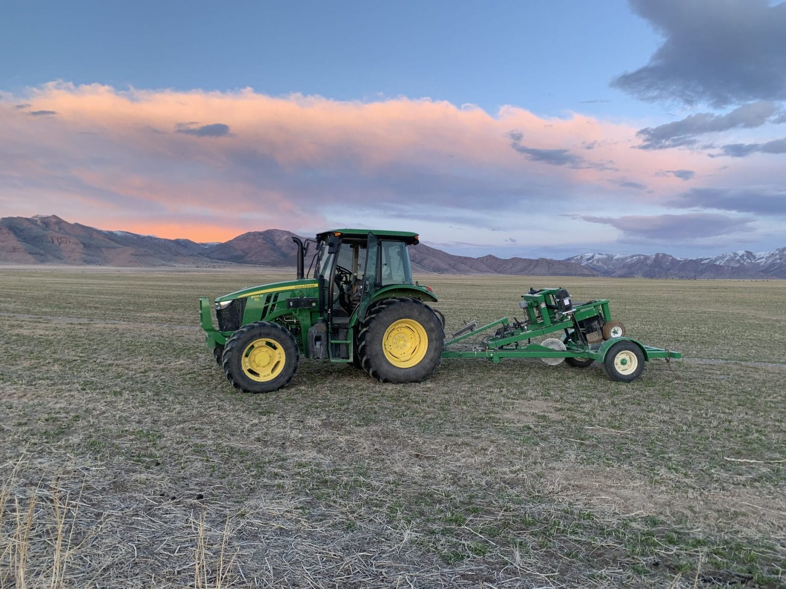 John Deere tractor in field beneath sunset mountain clouds
