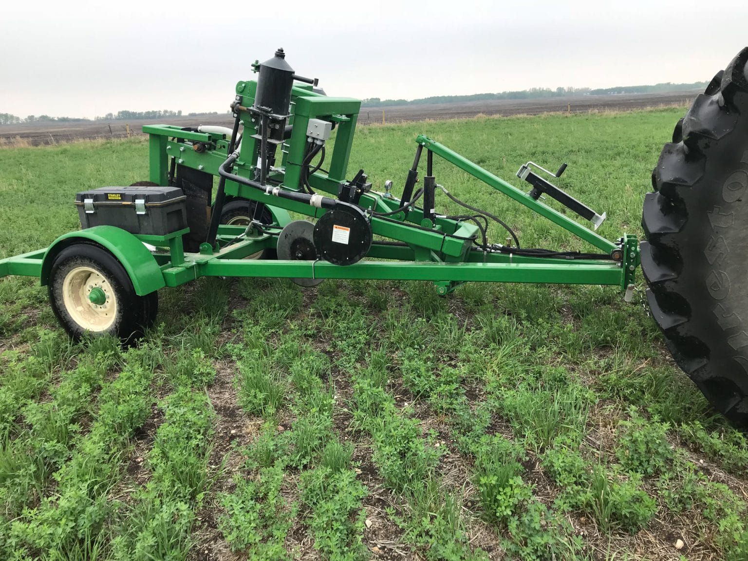 Green farm implement attached to tractor in grassy field