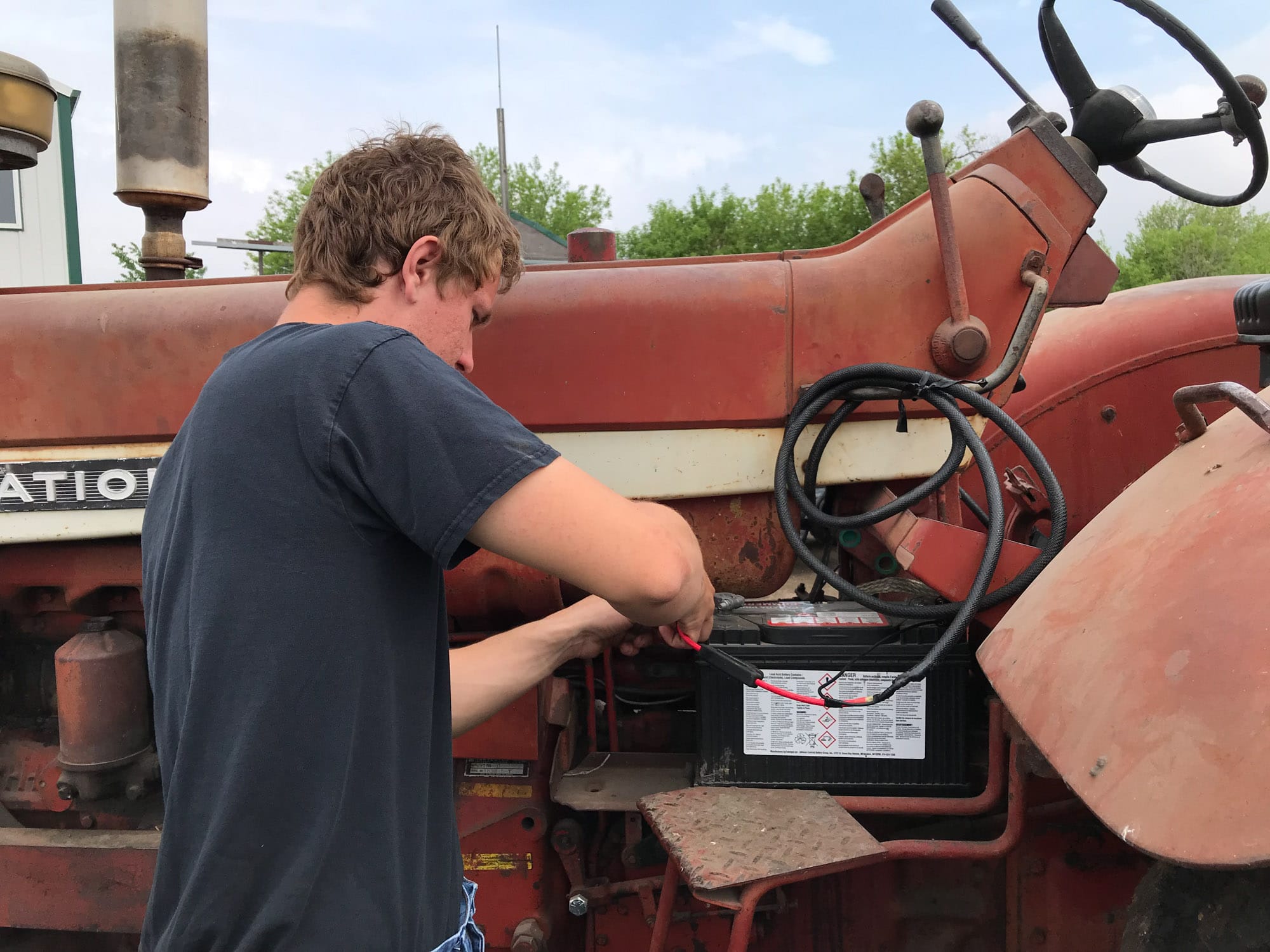 Person jump-starting battery on vintage red tractor