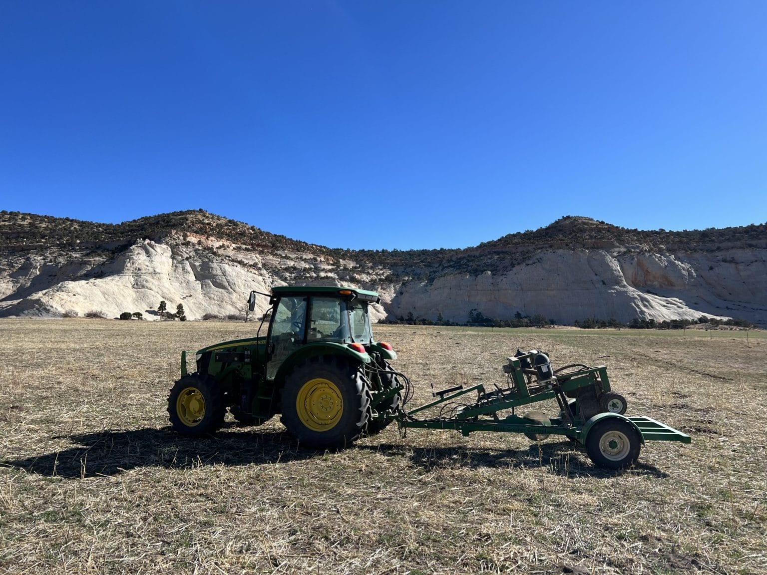 Green tractor in field beneath rocky hills and blue sky