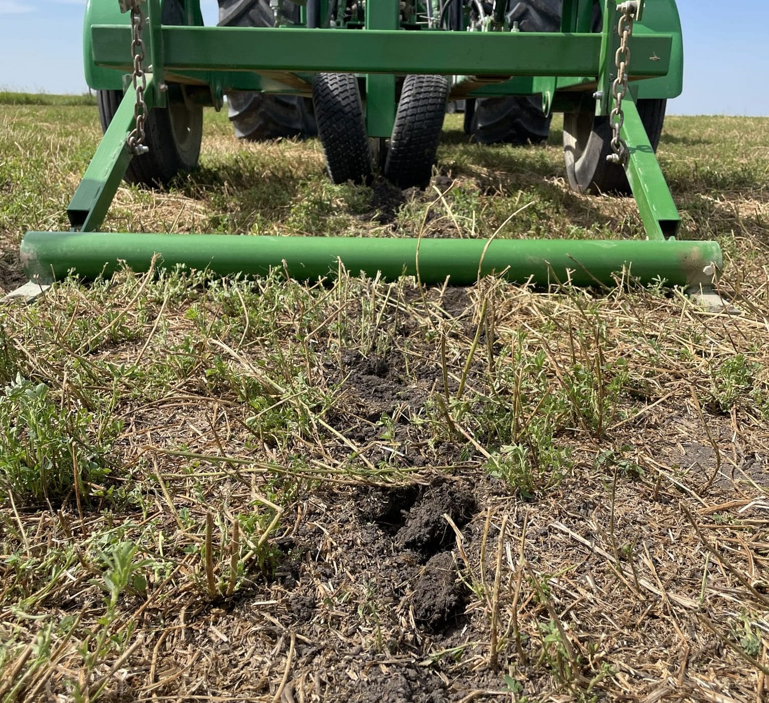 Green farm implement creating furrow in stubbly field