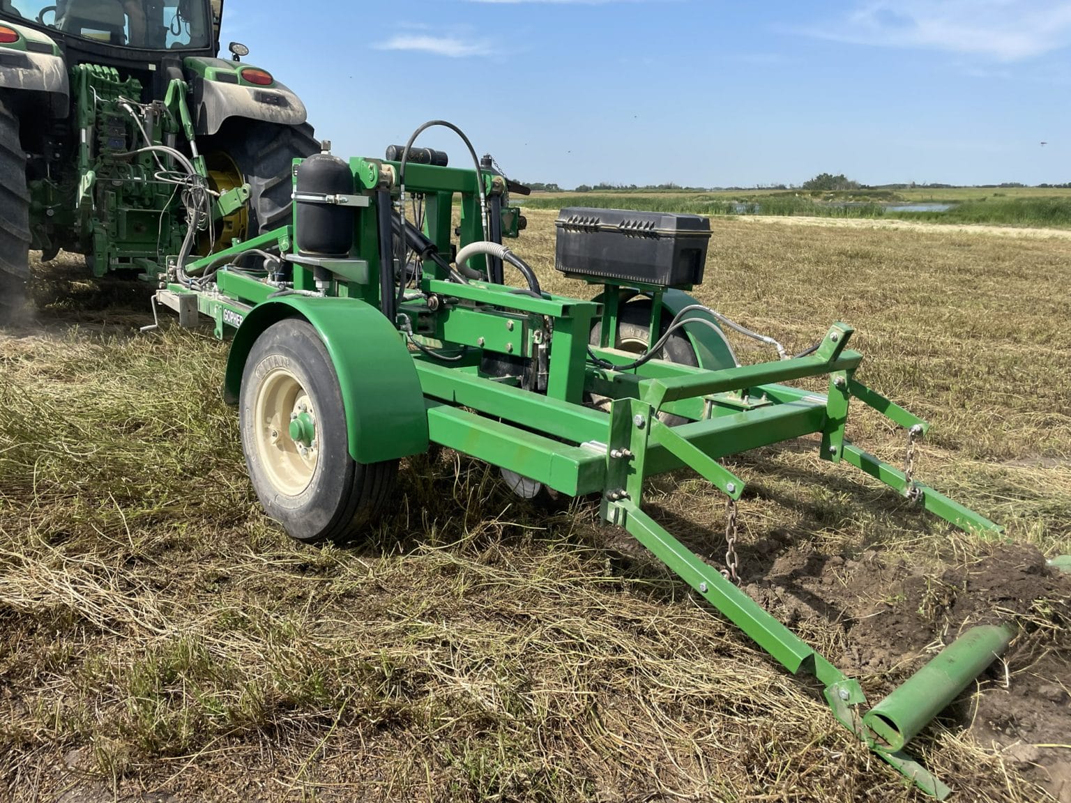 Green tractor-mounted farm implement in a harvested field