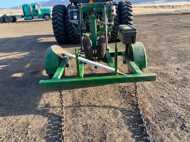 Green tractor-mounted agricultural implement with chains on gravel