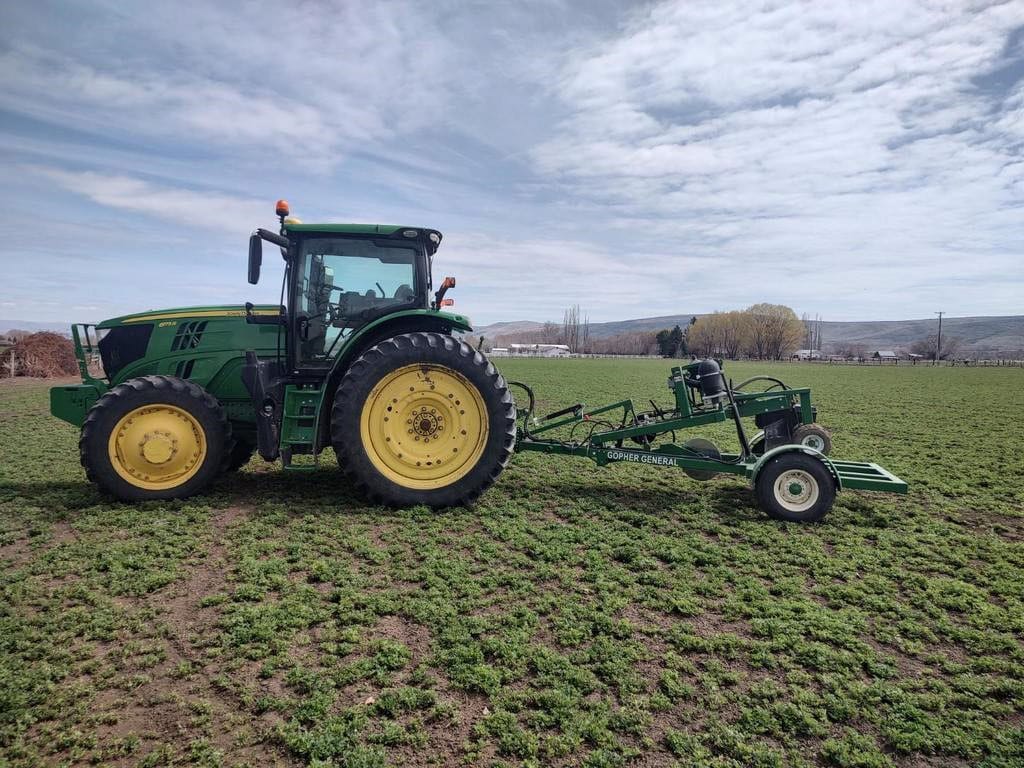 Green tractor pulling field implement across a young crop field