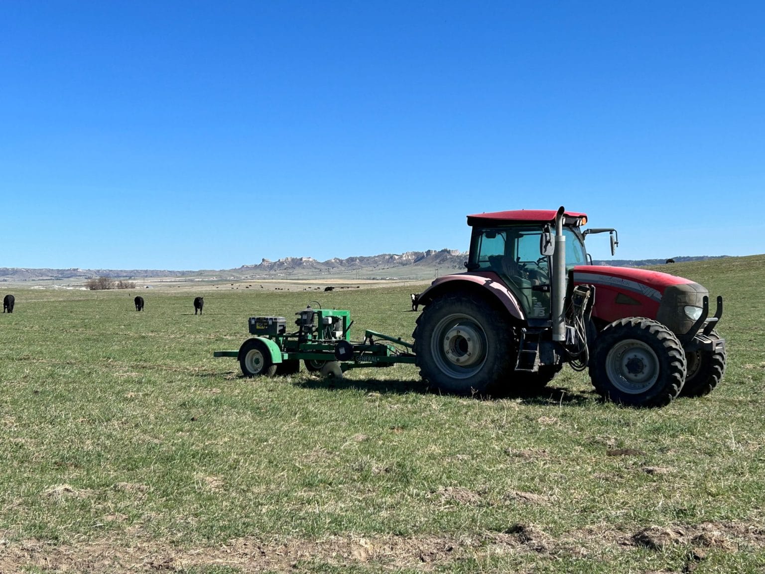 Red tractor in grassy pasture with cattle and distant hills